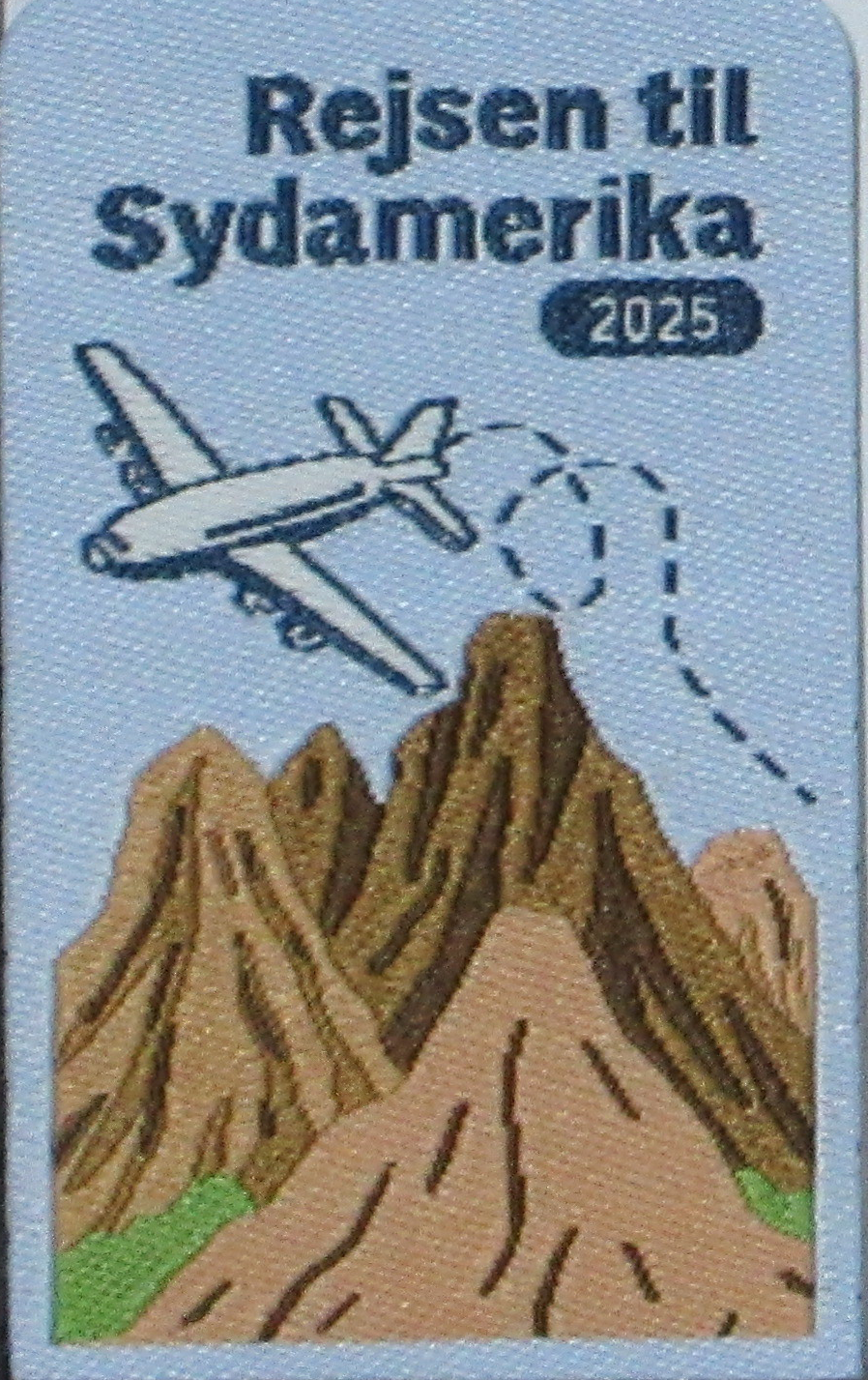 Vævet mærke 'Rejsen til Sydamerika 2025' med fly og bjerge